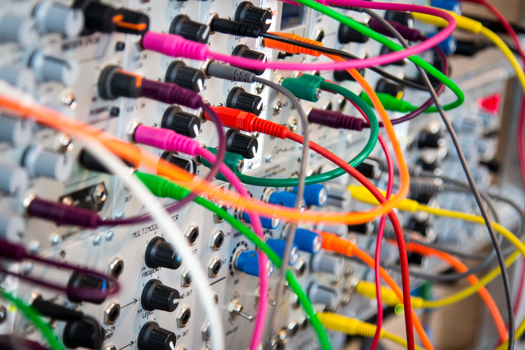 A modular synth patchbay: knobs, jacks, and a tangle of brightly coloured patch cables routing signal between modules.